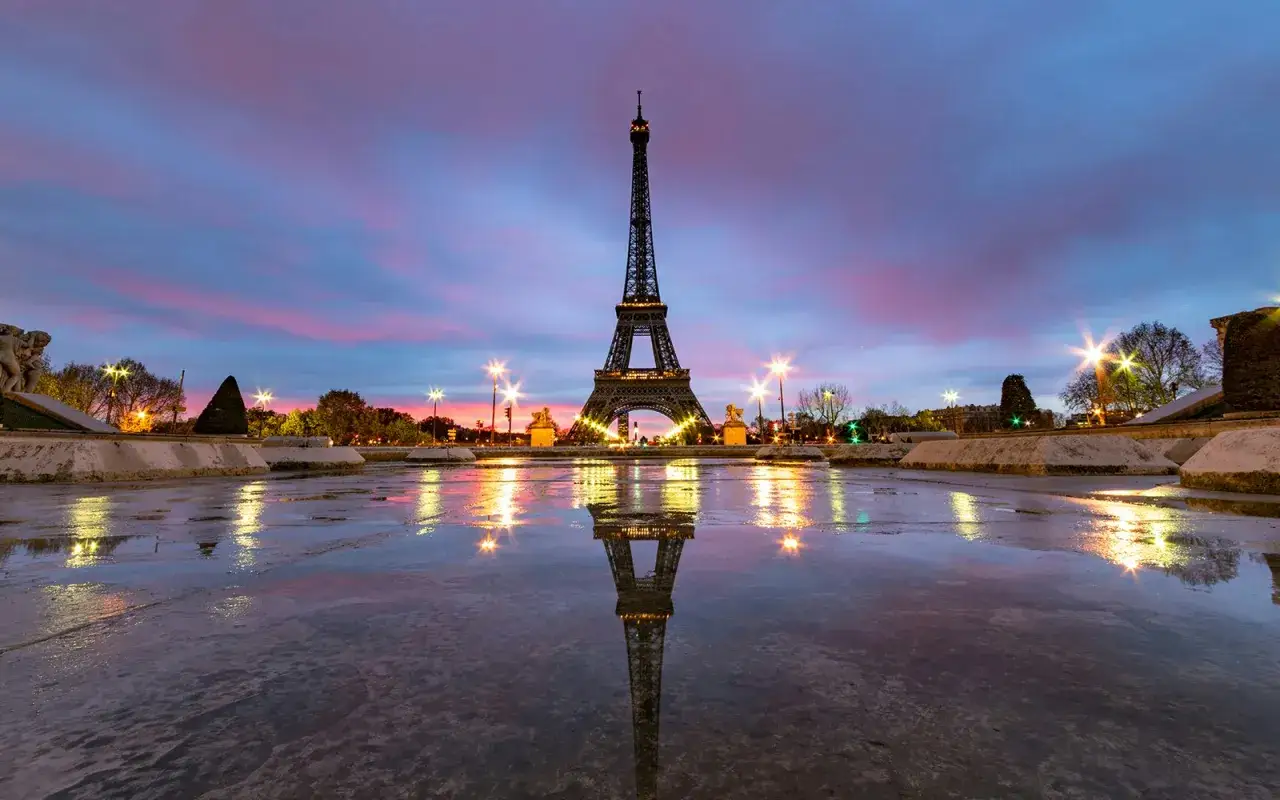 Wieża Eiffla o zmierzchu, odbijająca się w mokrej nawierzchni. Zastanawiasz się, ile kosztuje wejście na wieżę Eiffla?