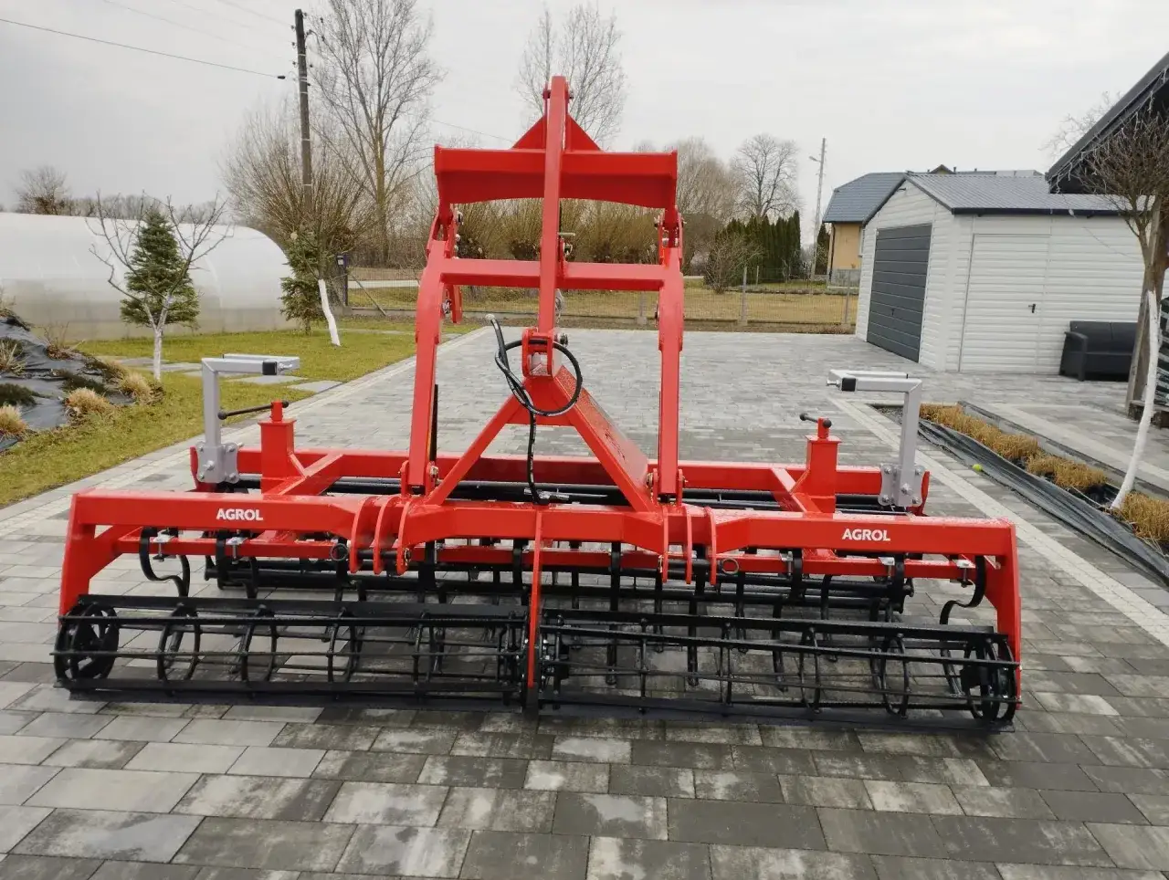 Czerwony mulczer do traktorka, gotowy do pracy na polu. Solidna konstrukcja z wałkami zagłębiającymi się w ziemię.