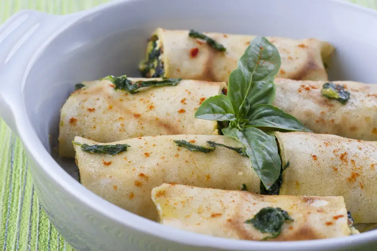 Roladki z mrożonego szpinaku w naleśnikach, posypane papryką, ozdobione bazylią. Prosty sposób, jak przyrządzić szpinak mrożony.