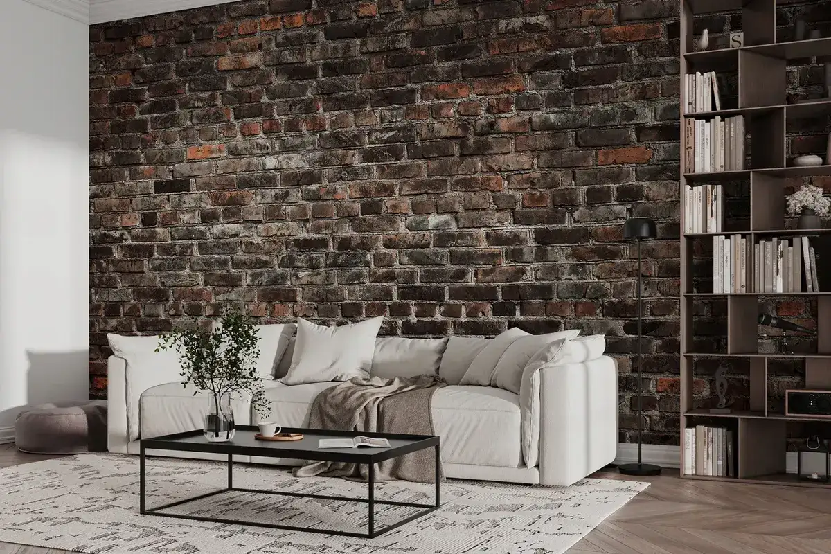 Nowoczesny salon z białą sofą i stolikiem kawowym na tle efektownej tapety czarna cegła. Obok regał z książkami.