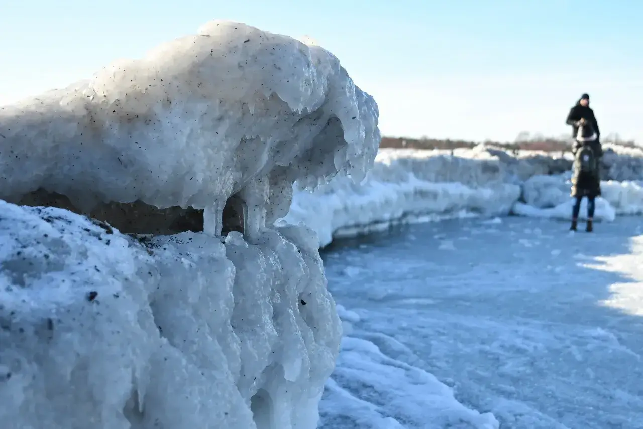 Lodowe formacje na brzegu, gdzie zamarza morze. W oddali widać dwie osoby spacerujące po zamarzniętej tafli.
