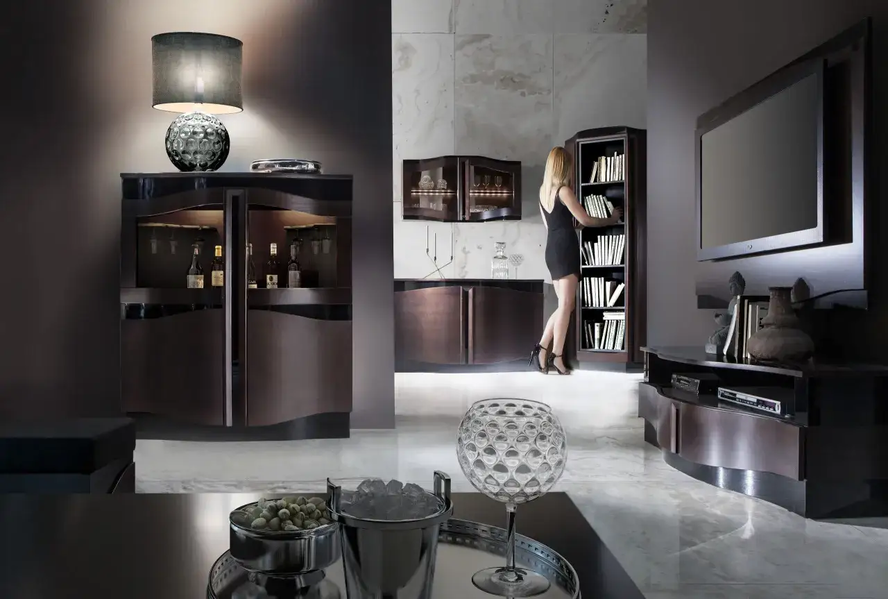 Eleganckie wnętrze z meblami w kolorze wenge. Kobieta w czarnej sukience wybiera książkę z regału.