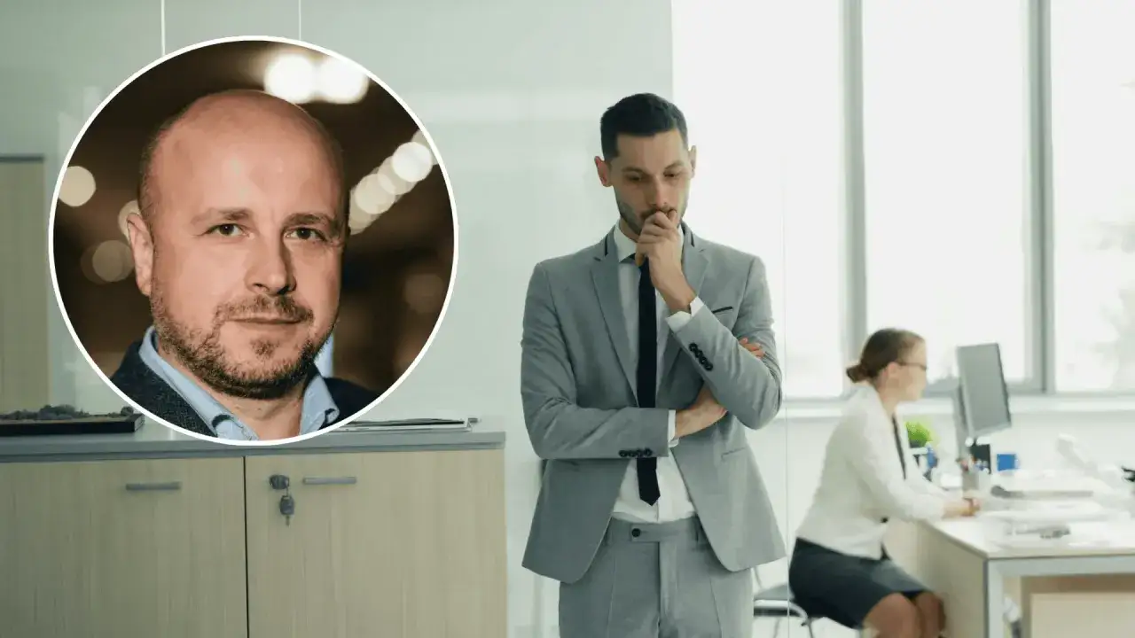 Mężczyzna w garniturze zastanawia się, jak sprawdzić nowego pracodawcę. W tle pracownica przy biurku.