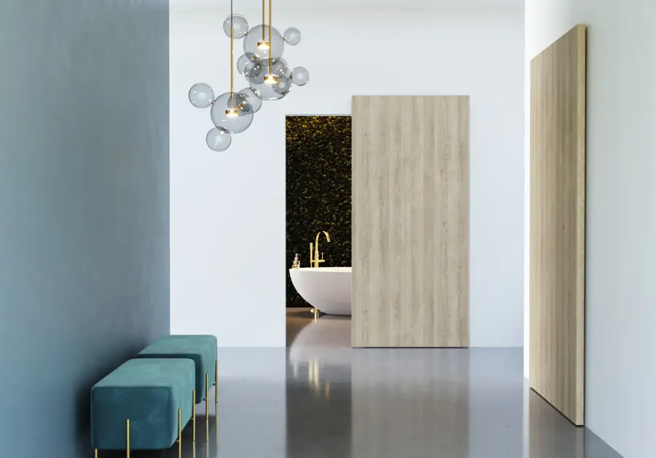 Nowoczesne wnętrze z wanną i złotą armaturą, do którego prowadzą drzwi przesuwne Porta. Dwa turkusowe pufy stoją przy niebieskiej ścianie.