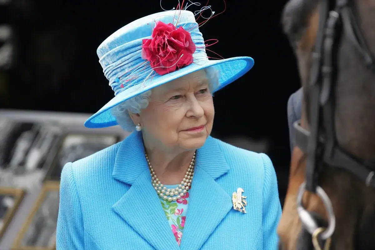 Królowa Elżbieta II w błękitnym kapeluszu i kostiumie, z perłowym naszyjnikiem. Zastanawiamy się, ile żyła królowa Elżbieta, patrząc na jej dostojną postać.