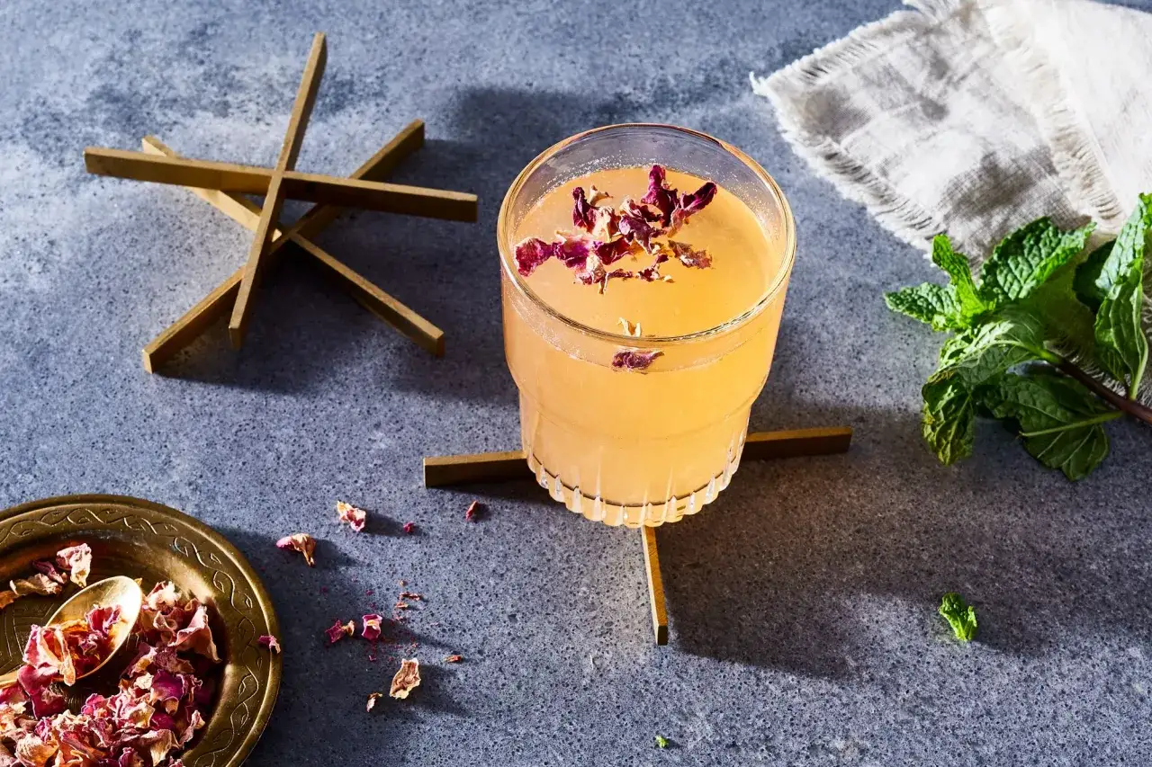 Elegancki drink z płatkami r&oacute;ży, idealny do domowych przepis&oacute;w na drinki. Obok świeża mięta i ozdobne elementy.