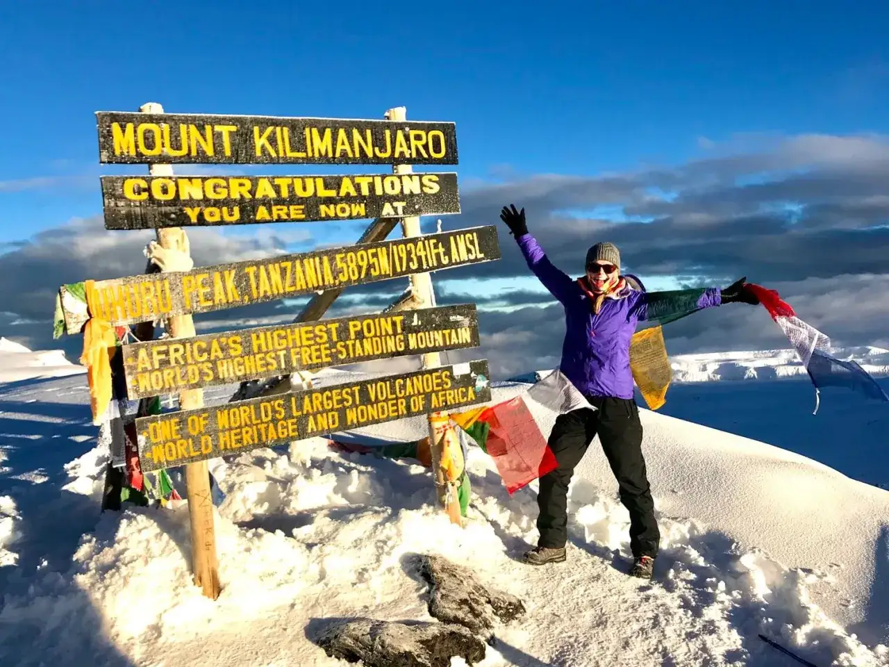 Szczęśliwa osoba na szczycie Uhuru Peak, najwyższy punkt Afryki. W tle tablica z napisem 