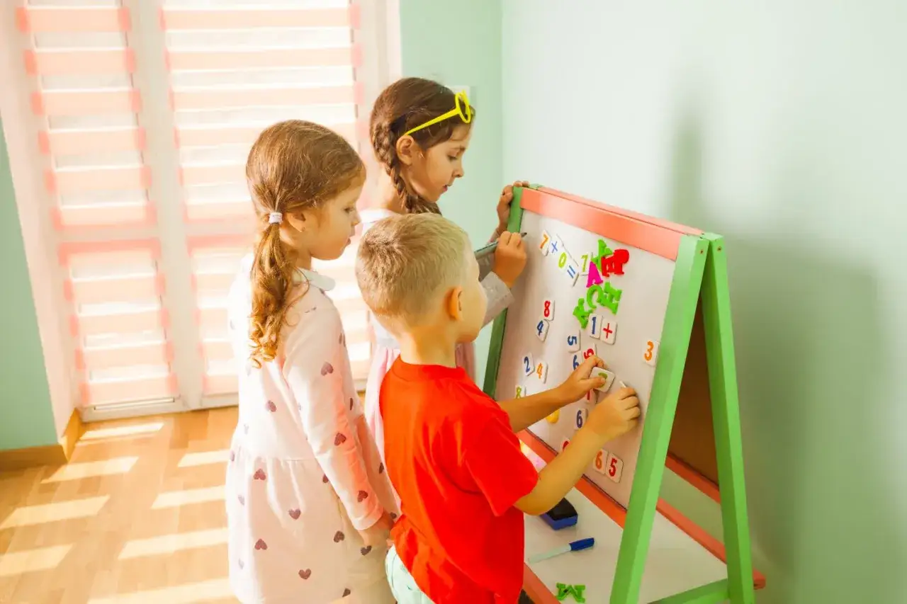 Dzieci uczą się matematyki, układając cyfry i znaki na tablicy. Zabawa z liczbami to świetny spos&oacute;b, jak nauczyć się matematyki.