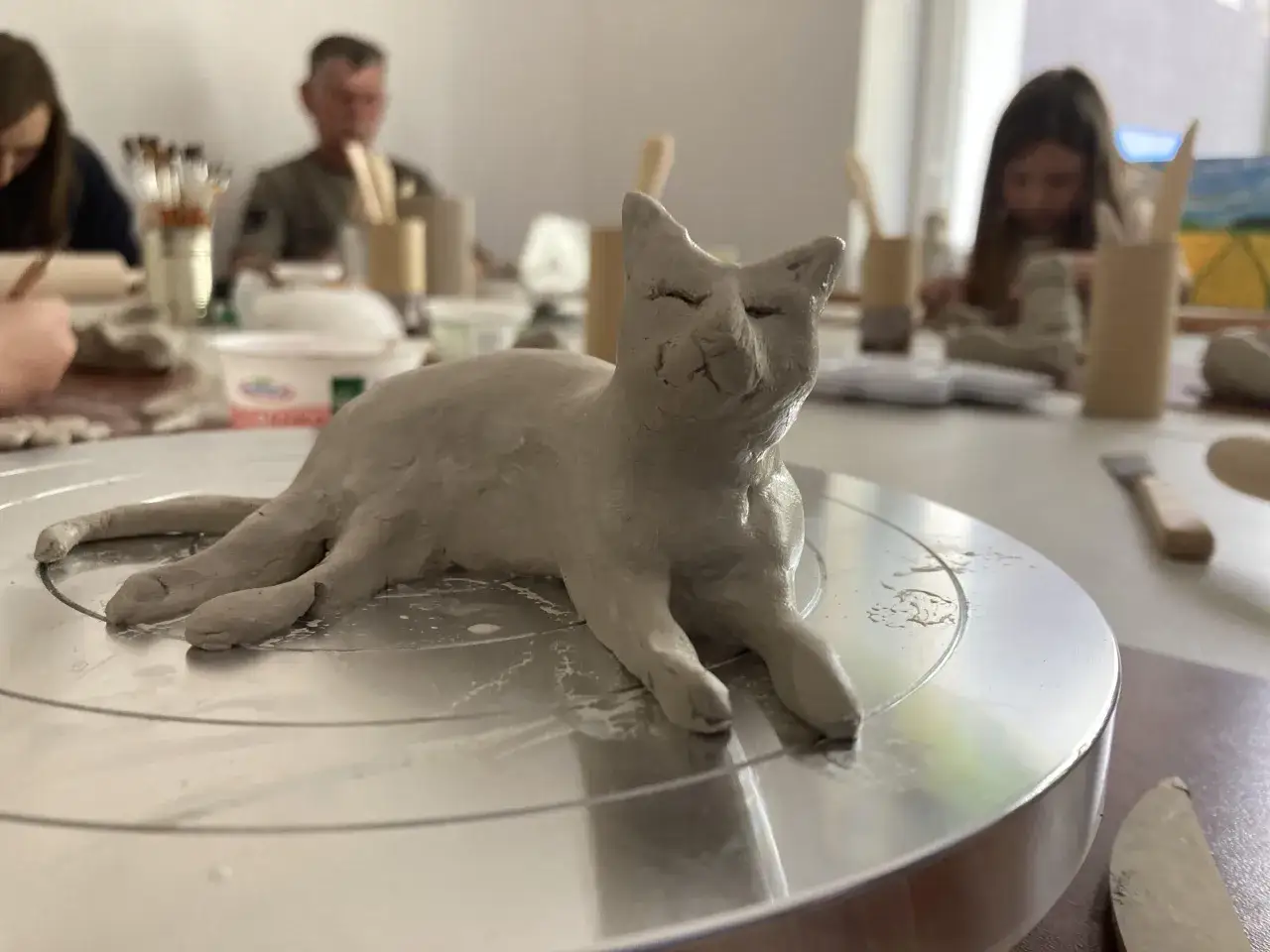 Uroczy kotek z gliny, efekt kreatywnego lepienia z gliny. W tle widać ludzi tworzących swoje dzieła.