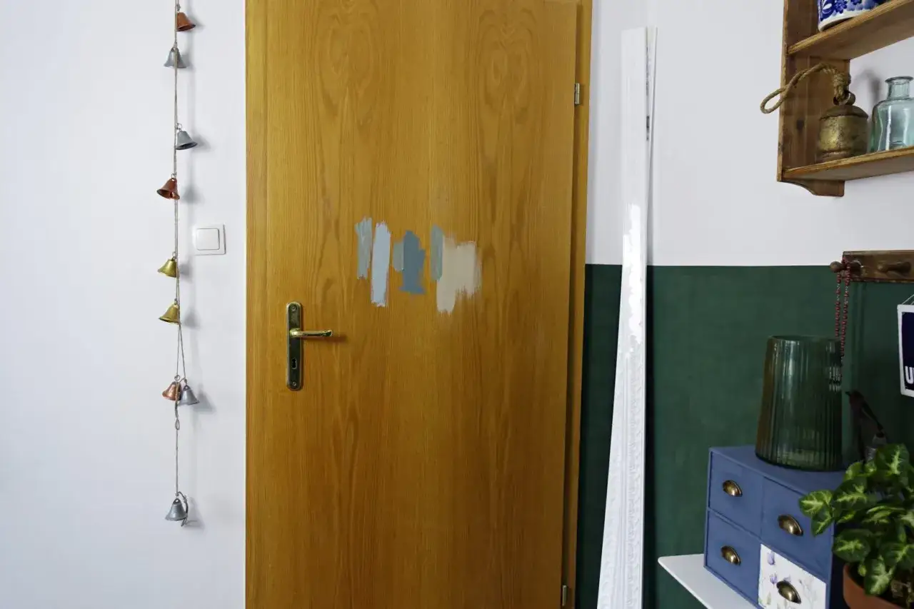 Próbki farb na drewnianych drzwiach z okleiny sugerują, że można je pomalować. Obok wisi sznur dzwoneczków.