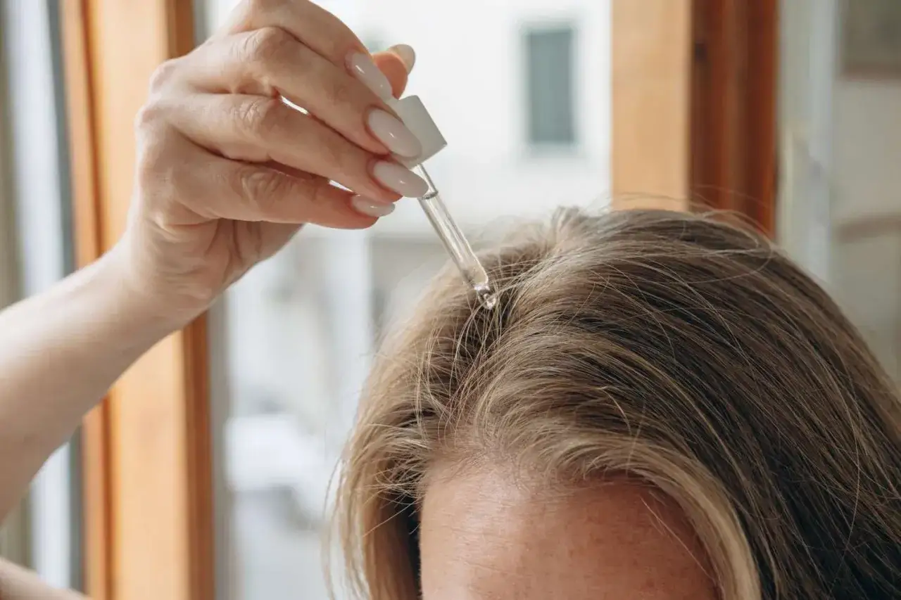 Dłoń z pipetką aplikuje serum na skórę głowy. To naturalny sposób na walkę z łupieżem, wykorzystujący moc octu.