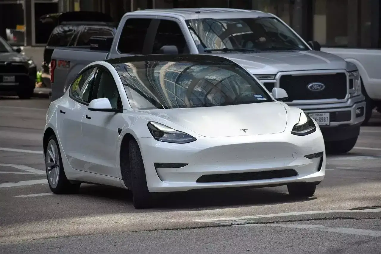 Biała Tesla na ulicy, obok Forda. Zastanawiasz się nad ubezpieczeniem OC Tesli? Sprawdź oferty!