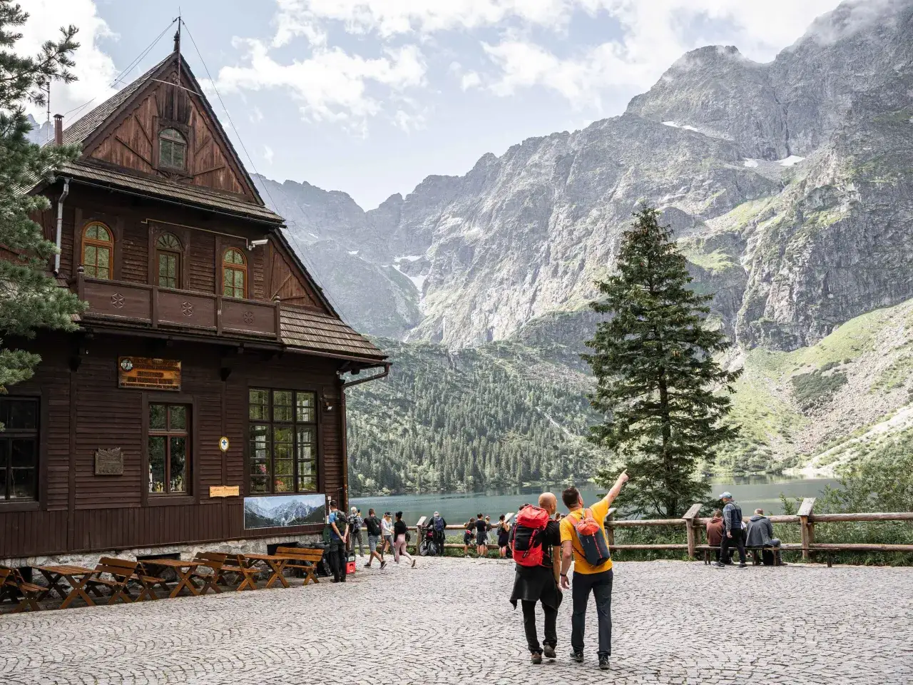 Gościna na wierchu: schronisko w g&oacute;rach, jezioro i skaliste szczyty. Turyści podziwiają widok.