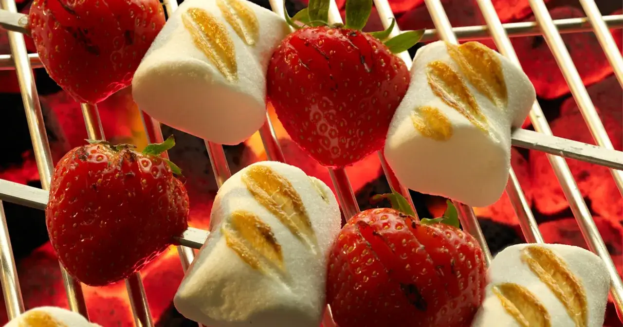 Słodki deser na grilla: truskawki i pianki nabite na szpadki, pieczone nad żarem.