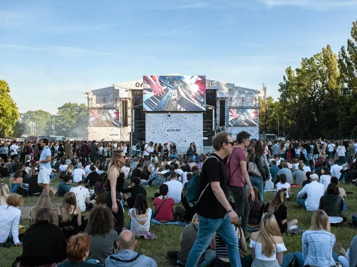 Tłum ludzi na trawie przed sceną, gdzie wyświetlane są wizualizacje. To jeden z największych festiwali muzycznych w Polsce.