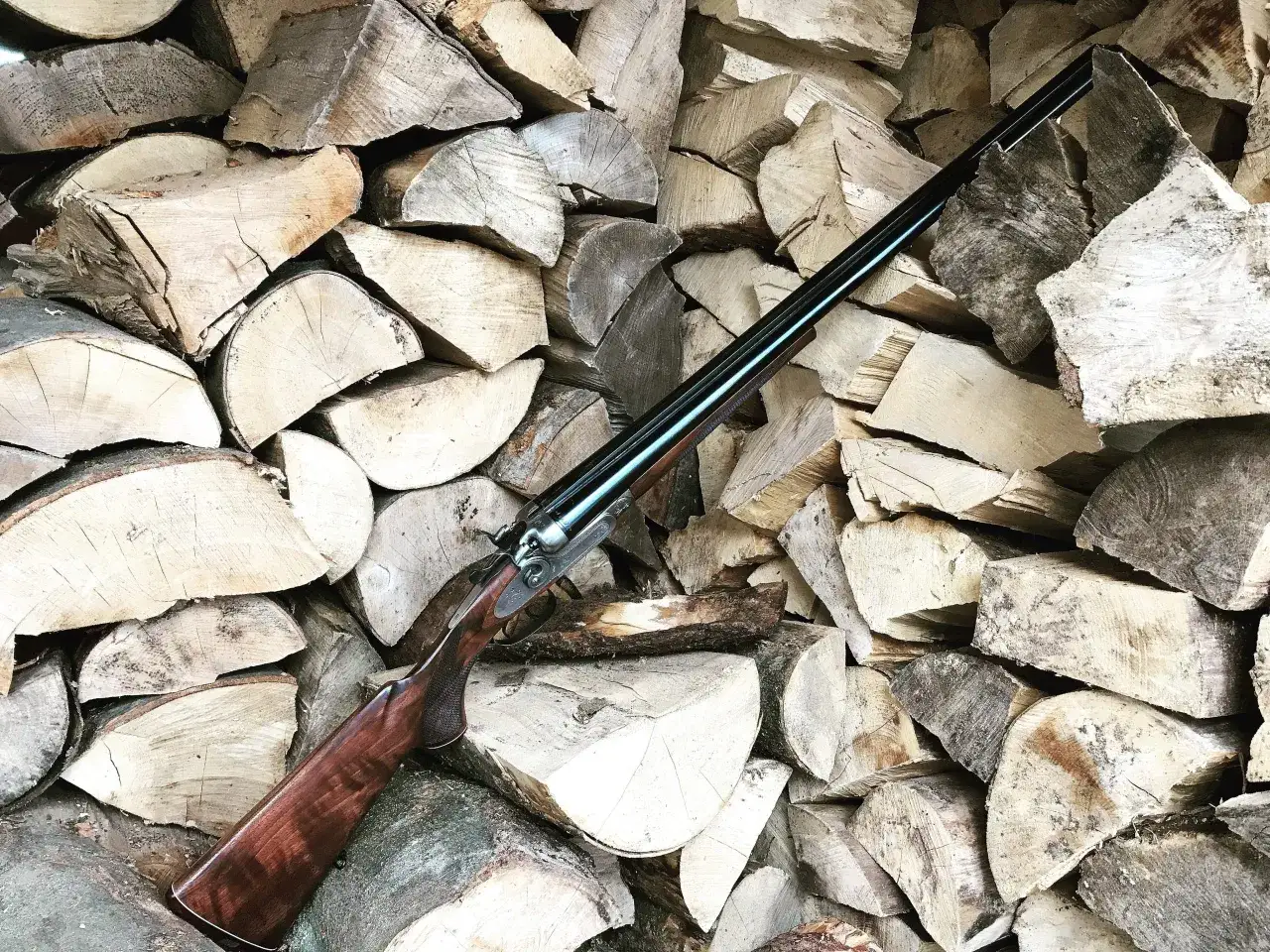 Dwulufowy dubeltówka na tle stosu drewna. Czy myśliwy może pożyczyć broń od kolegi?