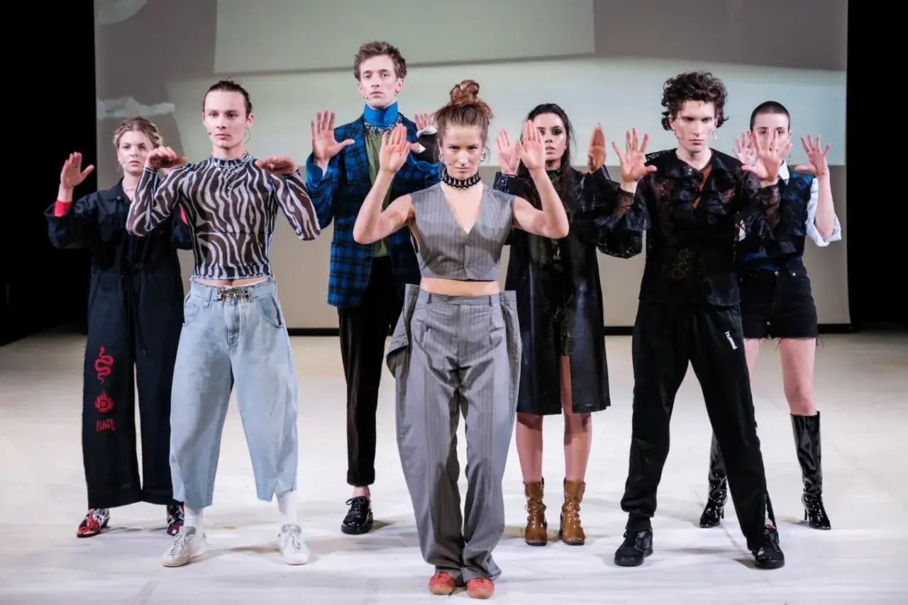 Grupa młodych ludzi w ekstrawaganckich strojach, z rękami uniesionymi w geście. To może być początek ich drogi, jak zostać aktorem.