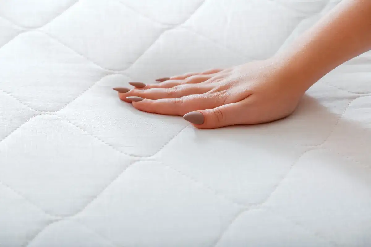 Dłoń dotyka białego, pikowanego pokrowca na materac.