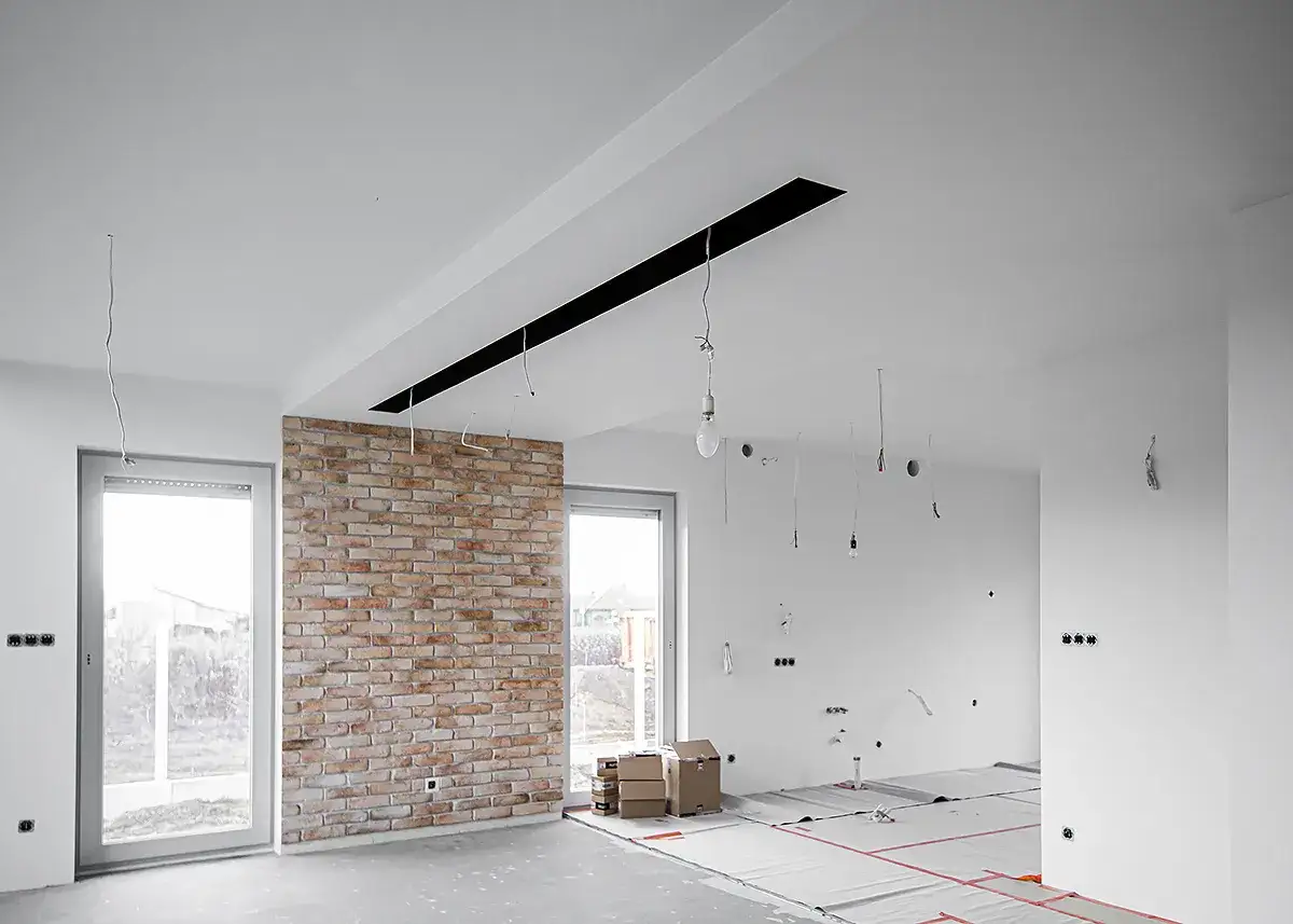 Nowe wnętrze z ceglaną ścianą i czarnymi pasami na suficie, czekające na wykończenie.