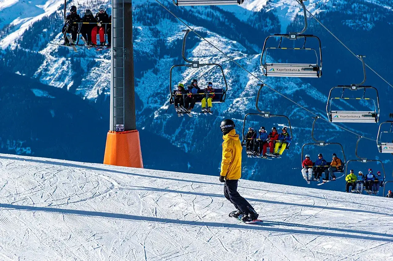 Snowboarder na stoku pod kolejką linową z narciarzami.