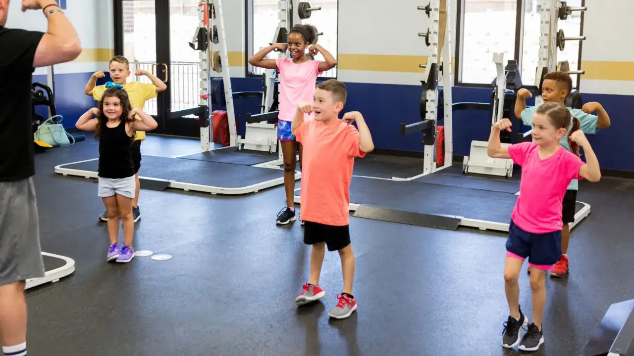 Dzieci ćwiczą z trenerem, który może prowadzić zajęcia sportowe z dziećmi. Pokazują swoje bicepsy, budując siłę i pewność siebie.