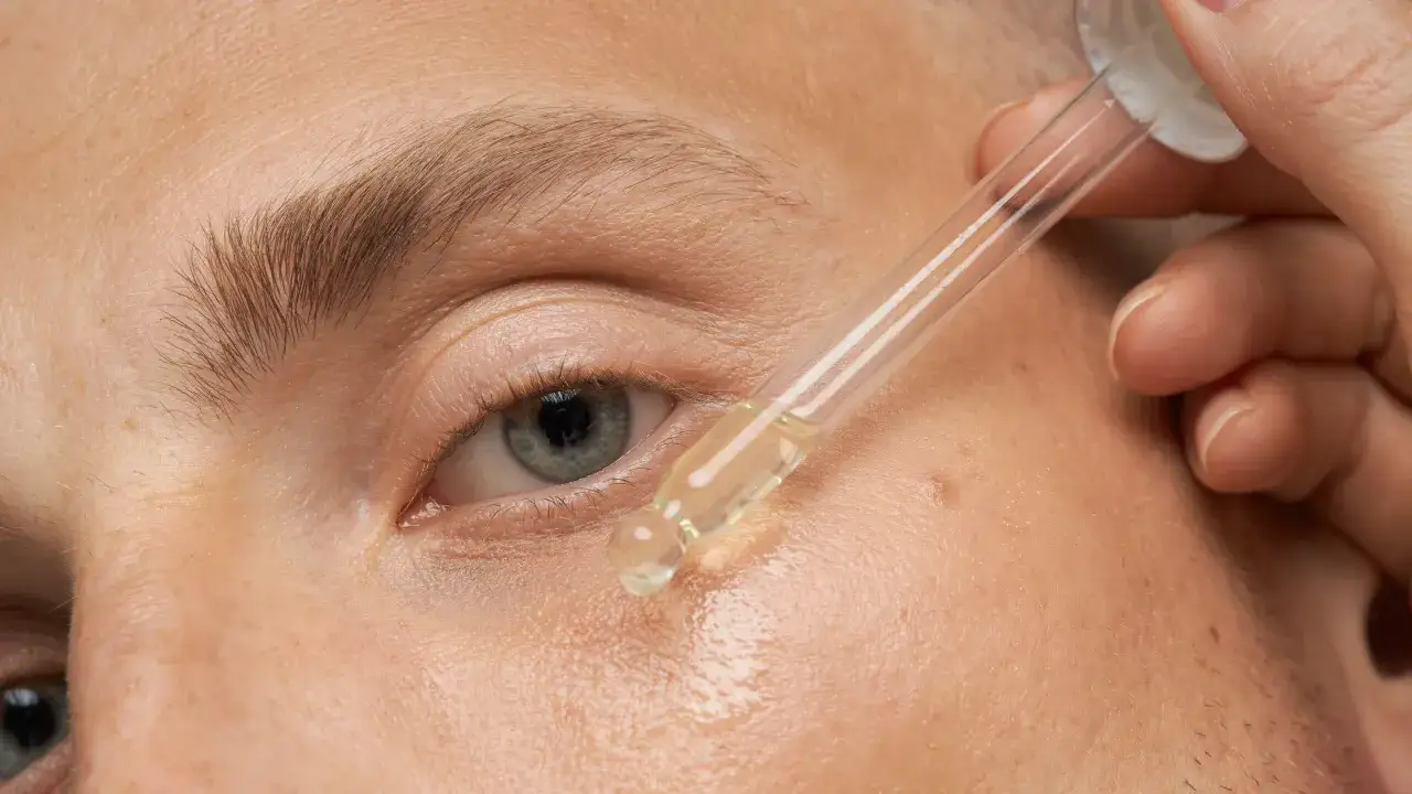 Nahaufnahme eines Auges, auf das ein Tropfen Öl aus einer Pipette aufgetragen wird.