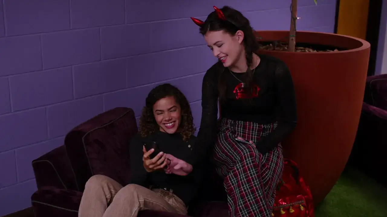 Uśmiechnięte dziewczyny przeglądają telefon, jak pisze zakochana dziewczyna, jedna z nich ma diabelskie rogi.