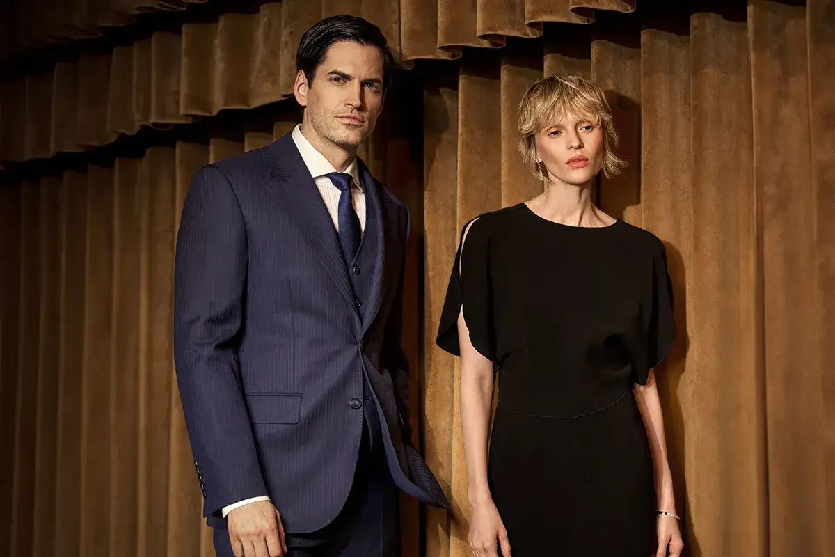 Mężczyzna w granatowym prążkowanym garniturze i kobieta w czarnej sukience. Klasyczna elegancja w modzie wizytowej, subtelna różnica między stylem old money a nowoczesnością.