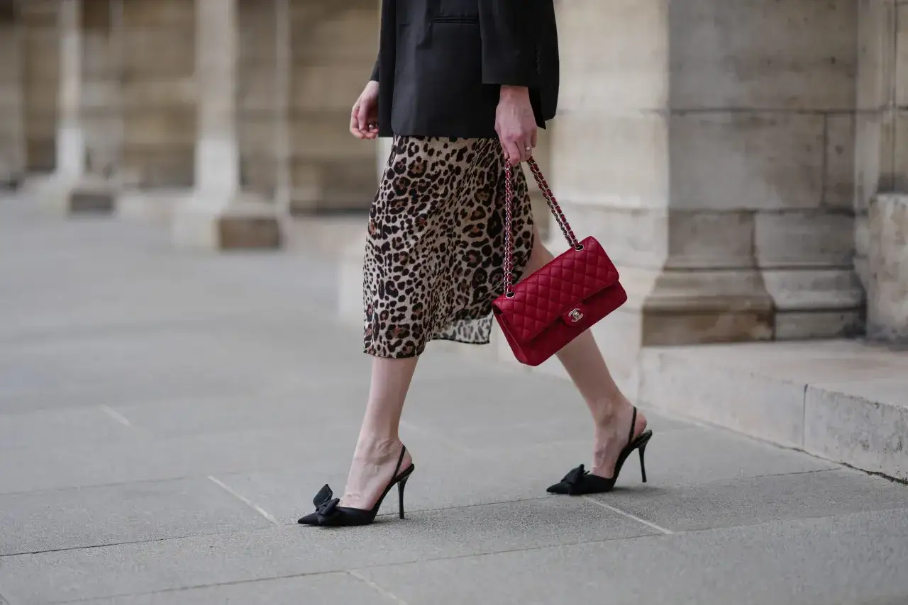 Elegancka kobieta w sukience w panterkę i czarnym blazerze, z czerwoną torebką Chanel. Czy sukienka w panterkę jest modna? Zdecydowanie tak!