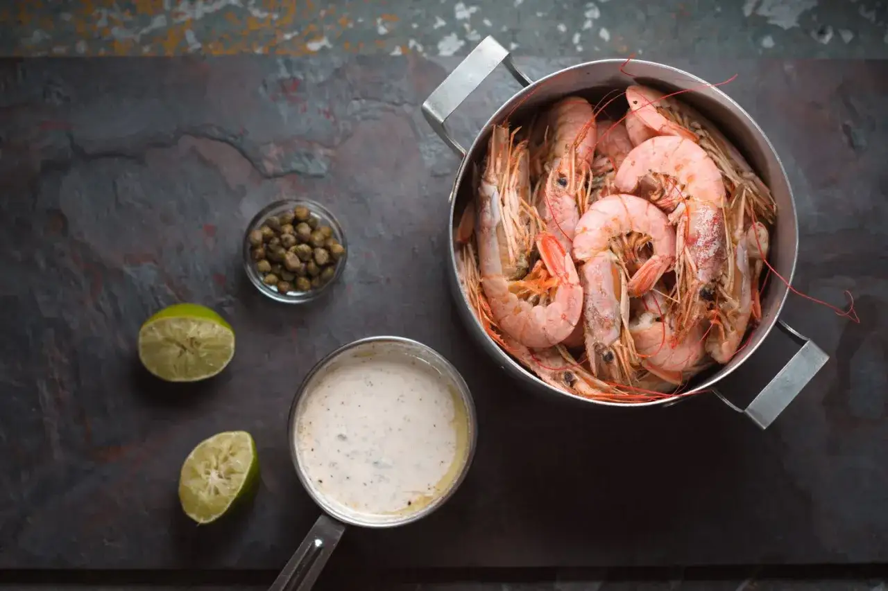 Gotowane krewetki w garnku, obok sos, kapary i limonka. Idealne do prostego przepisu na krewetki.