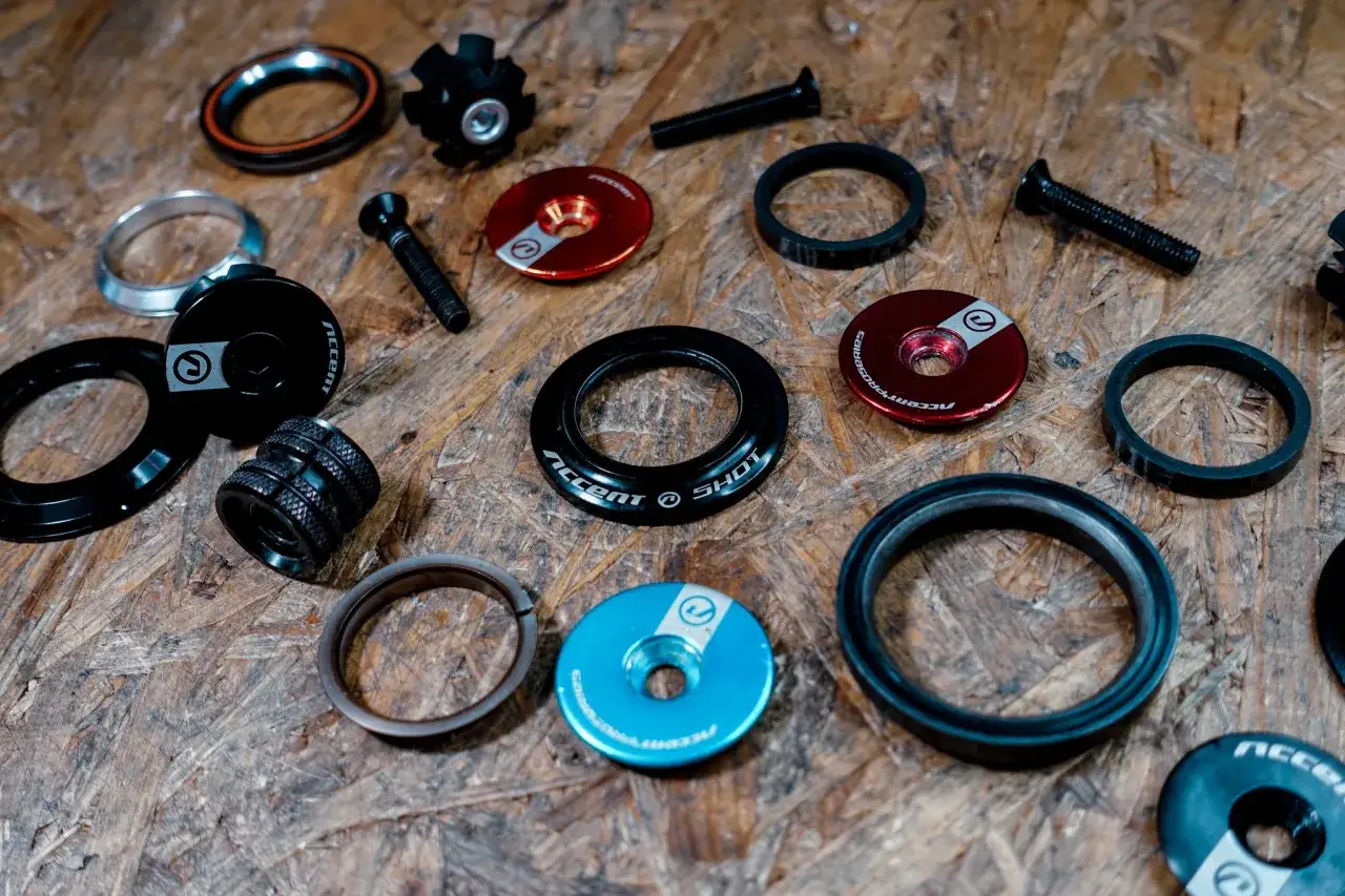 Zestaw części do sterów w rowerze: podkładki, kapsle, śruby i łożyska.