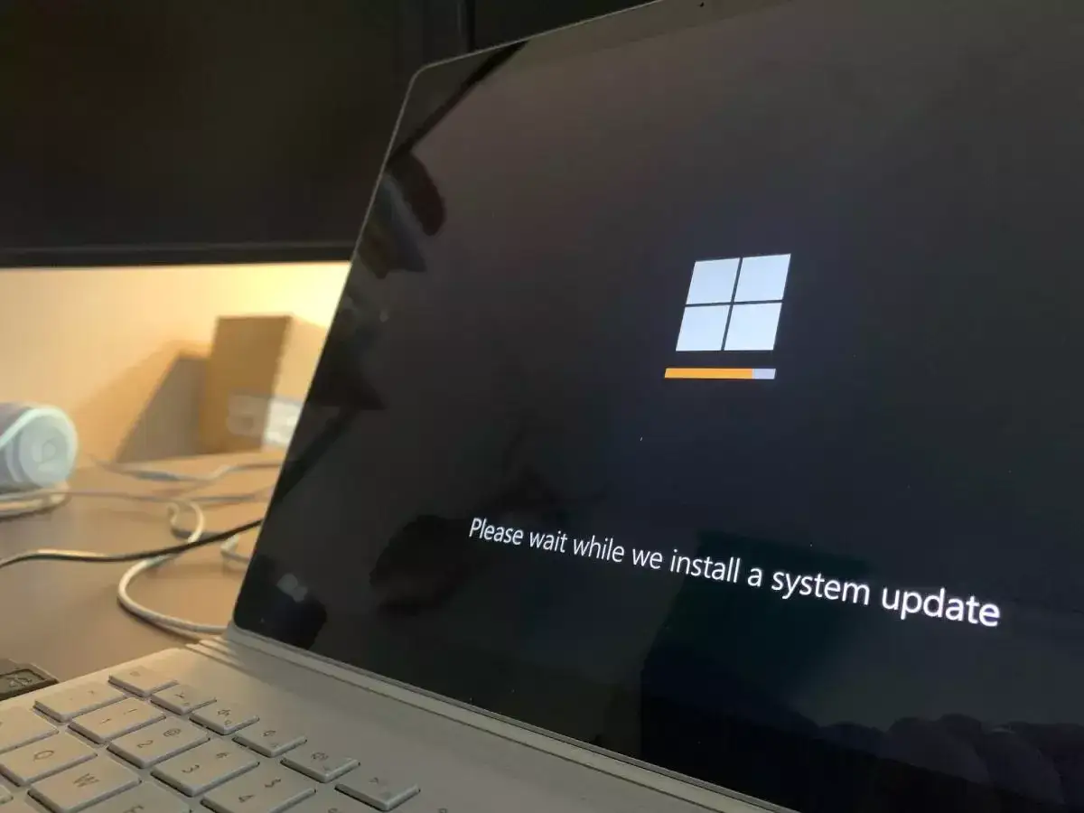 Ekran laptopa z logo Windows i komunikatem "Please wait while we install a system update". To ważny etap, jak aktualizować sterowniki, by system działał sprawnie.