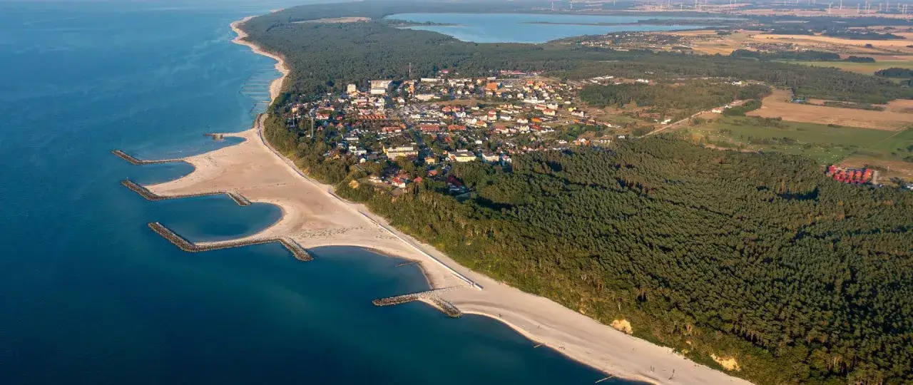 Widok z lotu ptaka na nadmorską miejscowość, gdzie jest Jarosławiec, z piaszczystą plażą, morzem i lasem sosnowym.