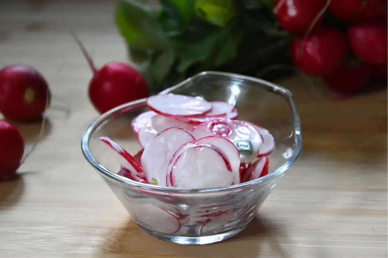 Pyszna surówka z rzodkiewki do obiadu, w szklanej miseczce, z kilkoma rzodkiewkami w tle.