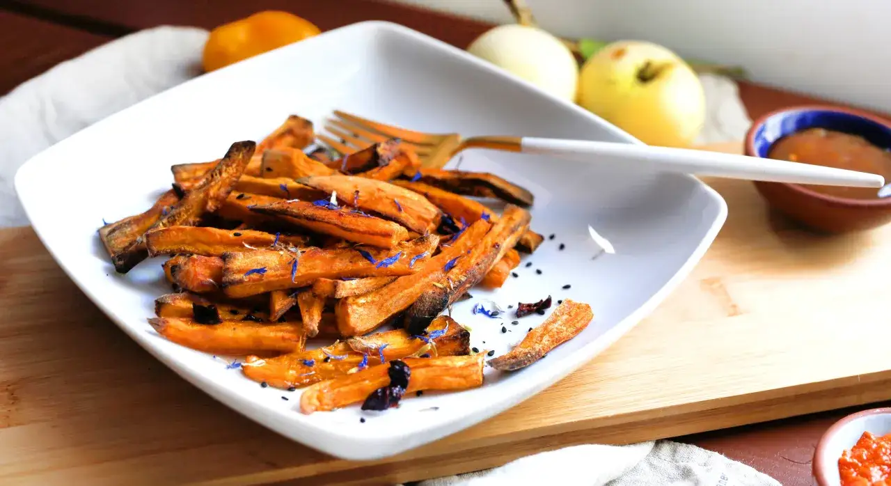 Chrupiące frytki z batatów na białym talerzu, posypane niebieskimi płatkami. Czy frytki z batatów są kaloryczne? Zależy od sposobu przygotowania!