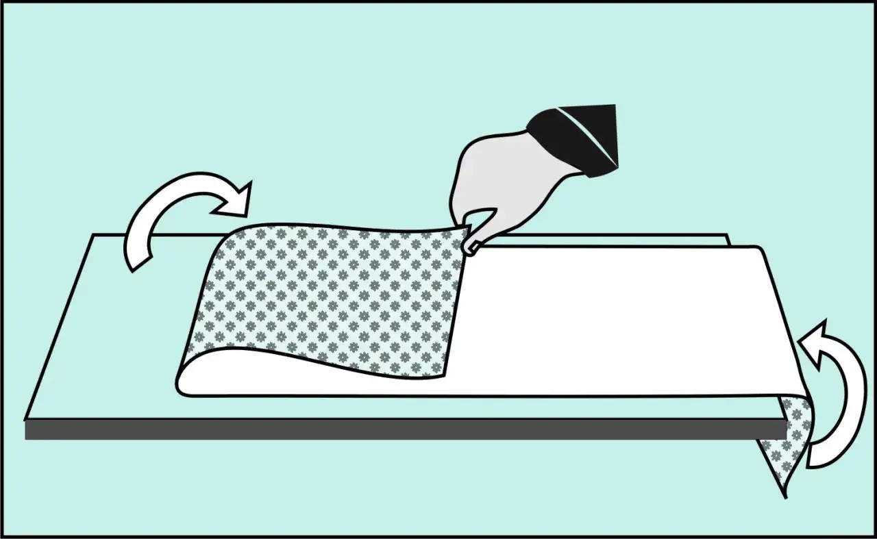 Ręka trzyma tapetę z wzorem kwiatowym, przygotowując ją do tapetowania przy otworach okiennych i drzwiowych. Strzałki wskazują kierunek składania.