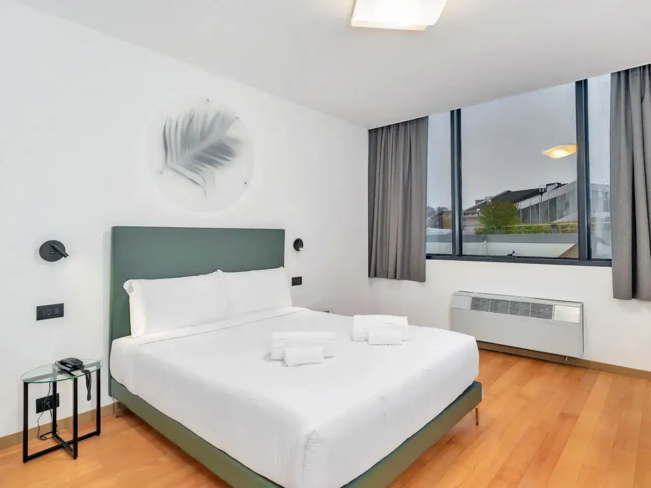 A modern hotel room with a king-size bed, white linens, and a green headboard.