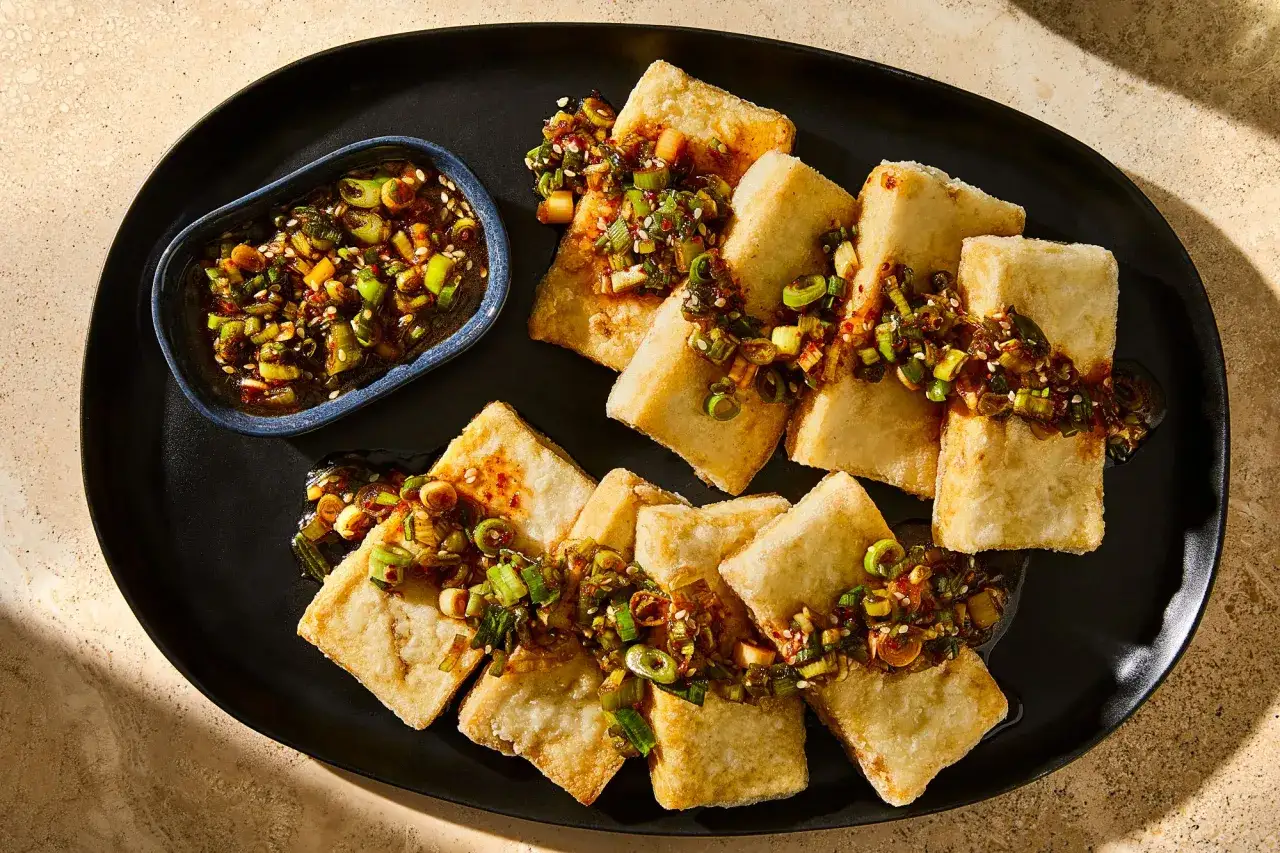 Chrupiące dania z tofu, polane aromatycznym sosem z dymką i sezamem, podane na czarnym talerzu.