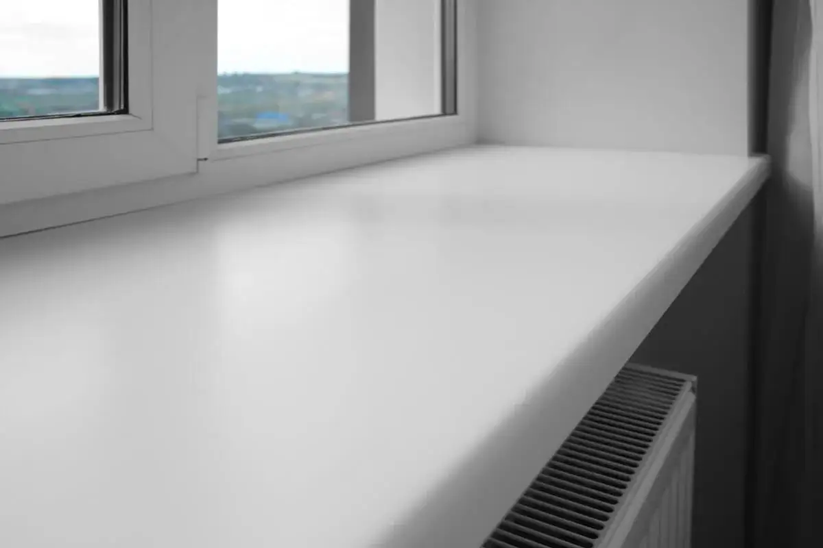 Biały, szeroki parapet okienny z tworzywa sztucznego, pod którym widać grzejnik. Czy parapet jest konieczny? To pytanie zadaje sobie wielu, ale ten dodaje funkcjonalności.