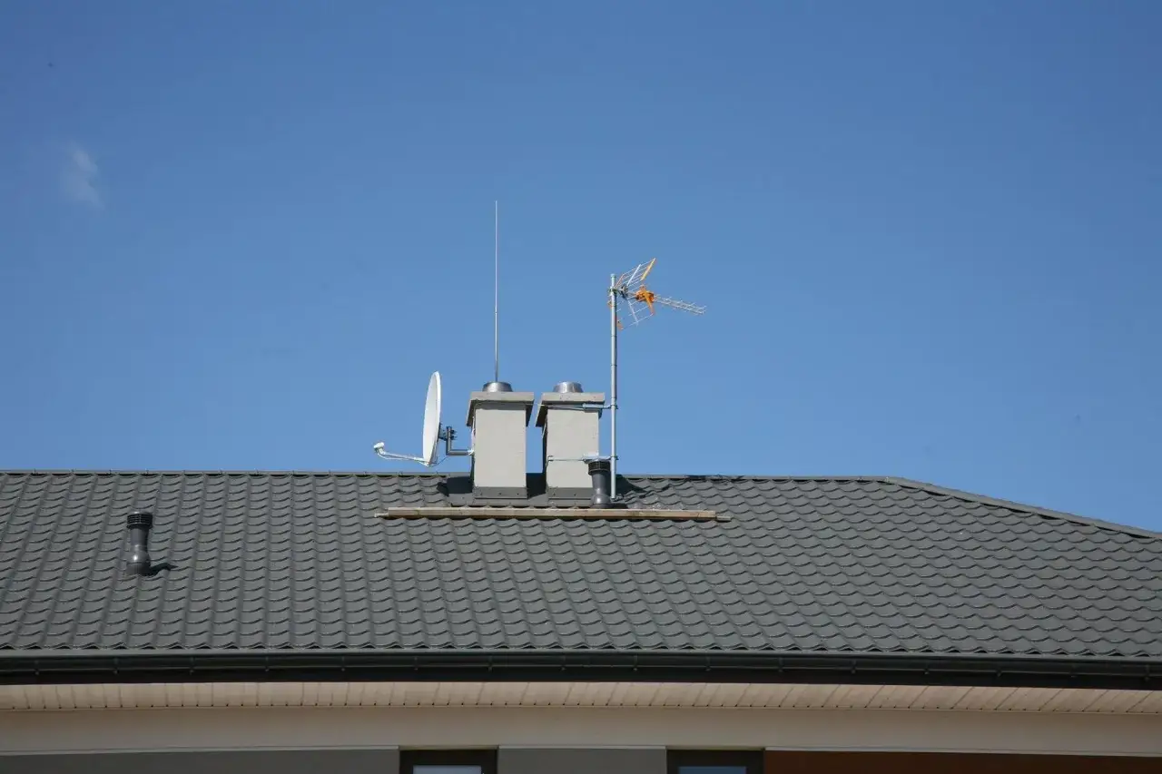 Dwa kominy na dachu z antenami. Zastanawiasz się, ile kosztuje szlamowanie komina?