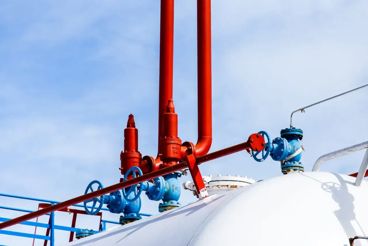 Czerwone i niebieskie zawory na białym zbiorniku na gaz. Zastanawiasz się, na ile wystarcza zbiornik na gaz 2700?