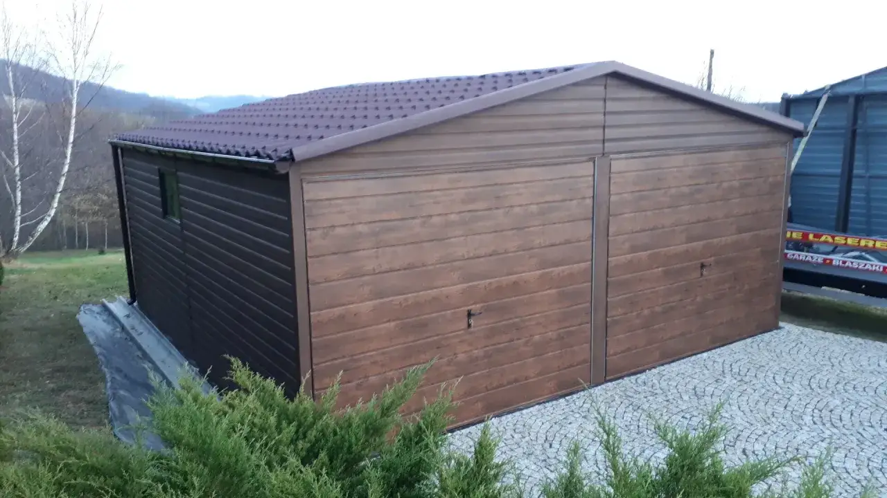 Nowoczesny garaż z dachem jednospadowym, imitującym drewno, z dwoma bramami uchylnymi. Otoczony zielenią i brukowanym podjazdem.