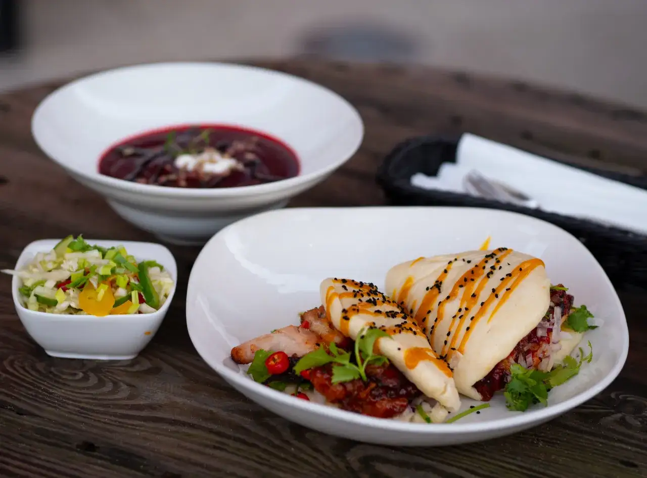 Talerze z zupą, sałatką i bułeczkami bao z mięsem na drewnianym stole.