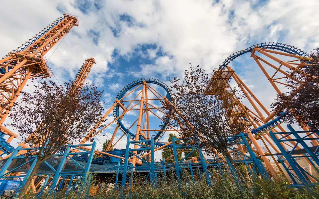 Montaña rusa naranja y azul con cielo nublado.