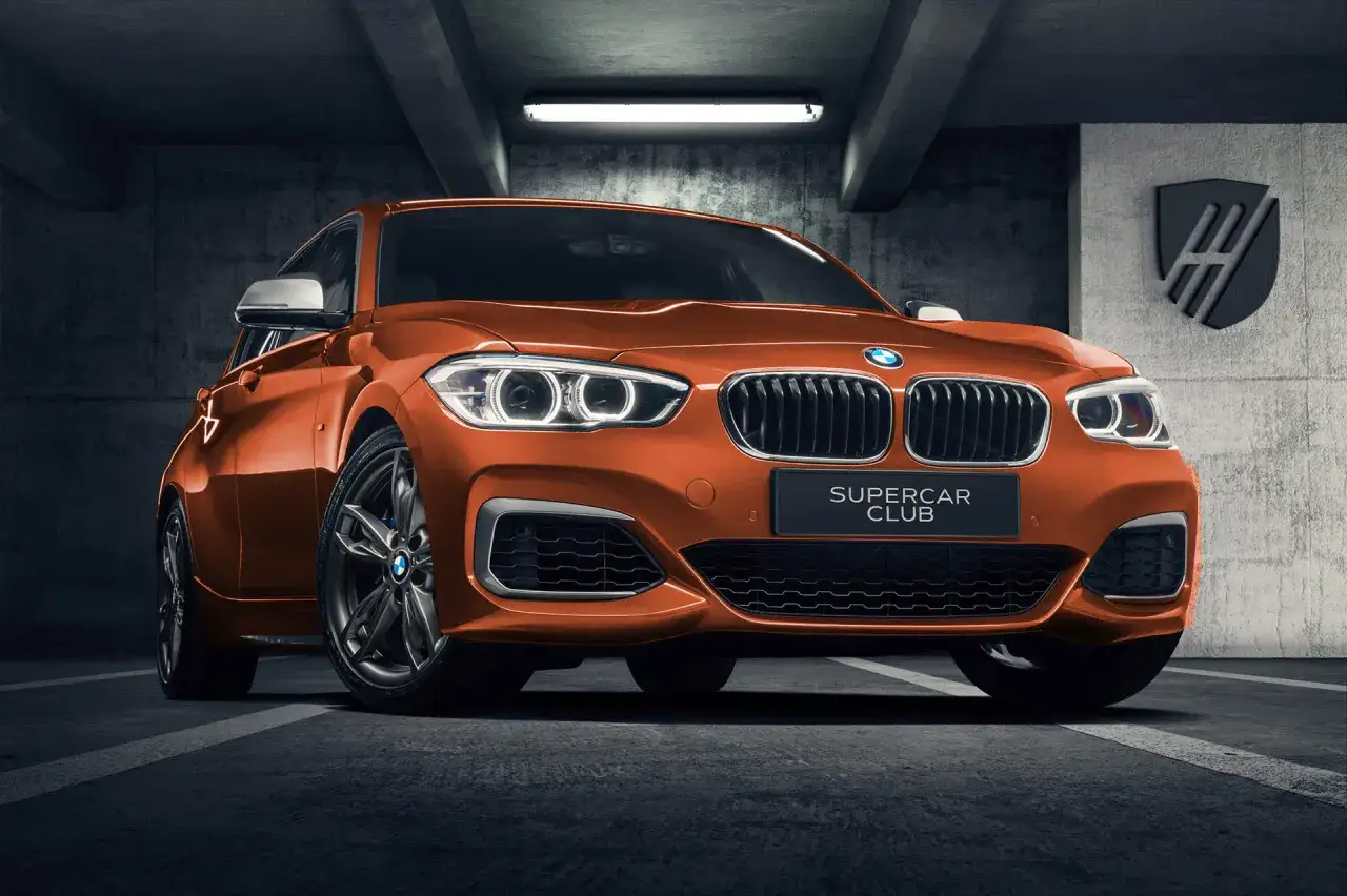 Pomarańczowe BMW 140i z tabliczką "SUPERCAR CLUB" stoi w garażu.
