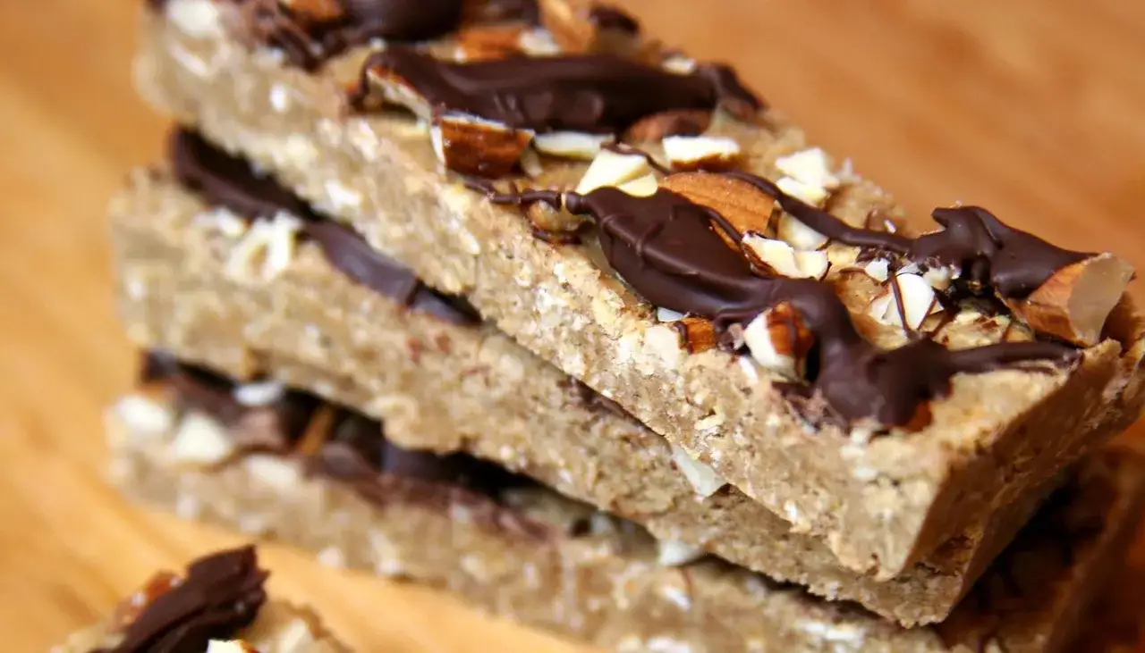Stos batonów proteinowych z czekoladą i migdałami na drewnianym tle.