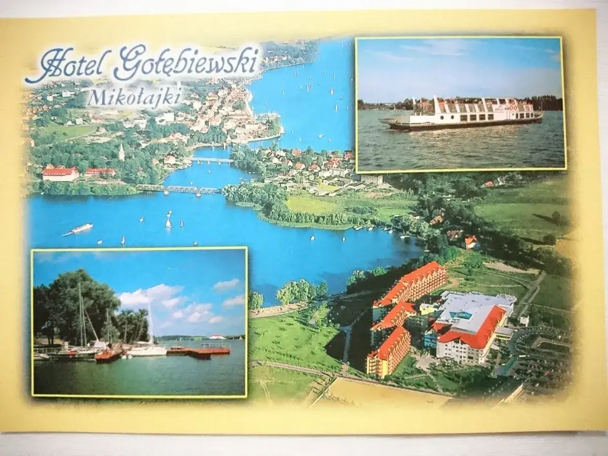 Widok na Hotel Gołębiewski w Mikołajkach i jezioro. Widoczny statek wycieczkowy i żaglówki.