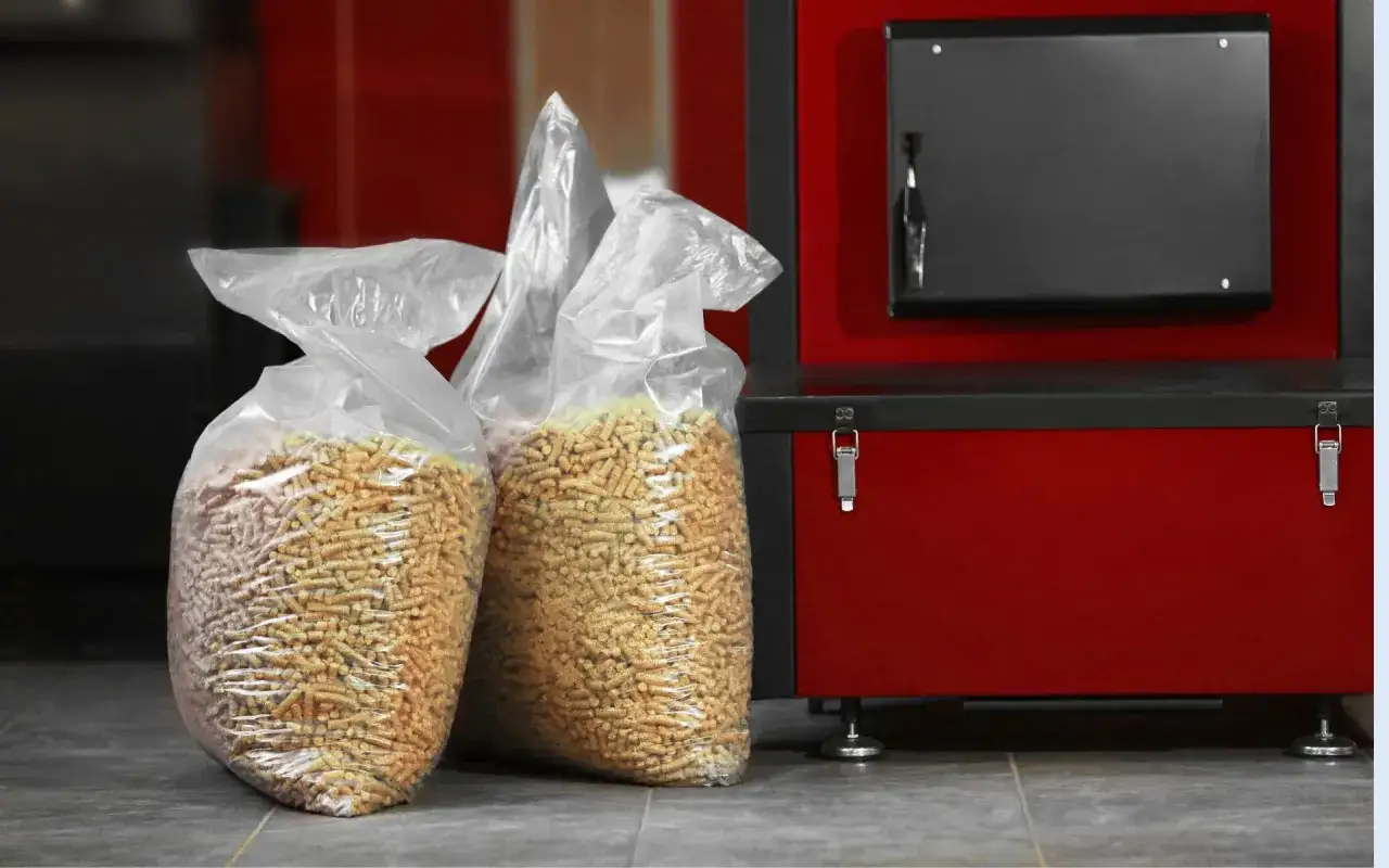 Dwie torby z pelletem drzewnym obok czerwonego pieca na pellet.