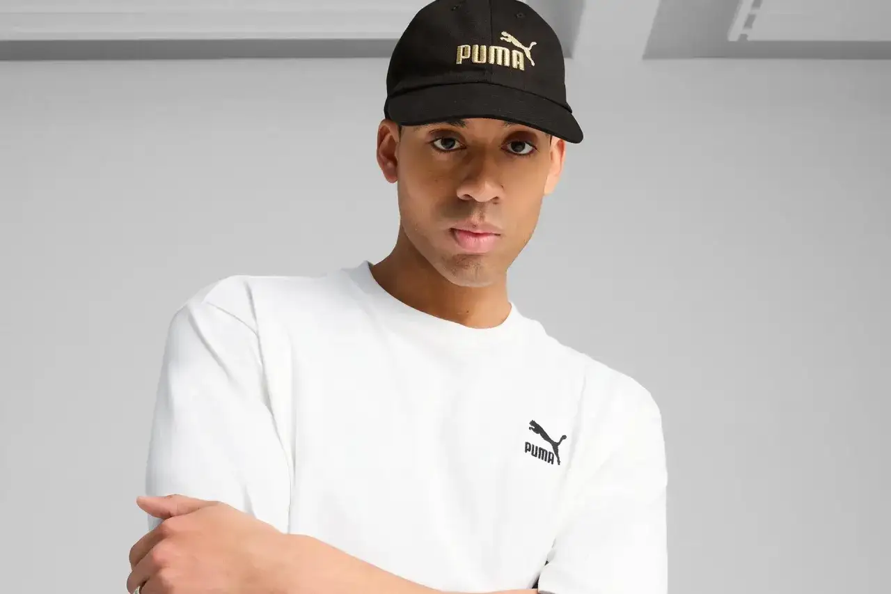 Mężczyzna w czarnej czapce z logo Puma i białej koszulce.