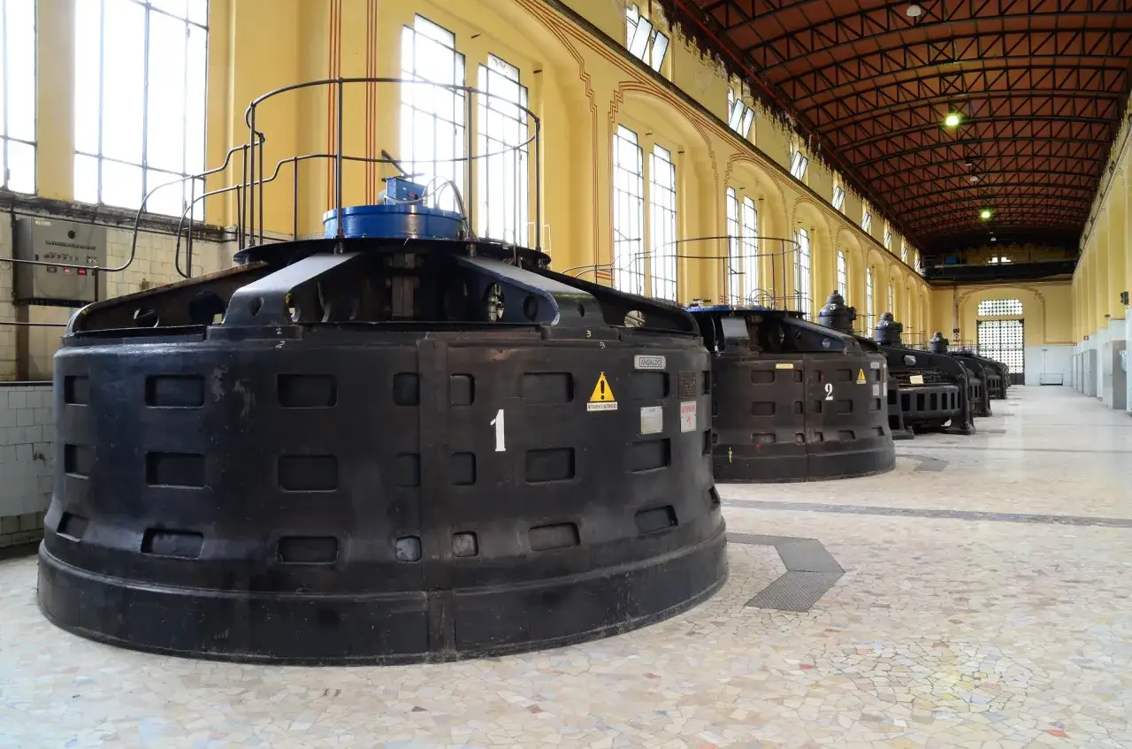 Wnętrze elektrowni z rzędem dużych, czarnych turbin wodnych.